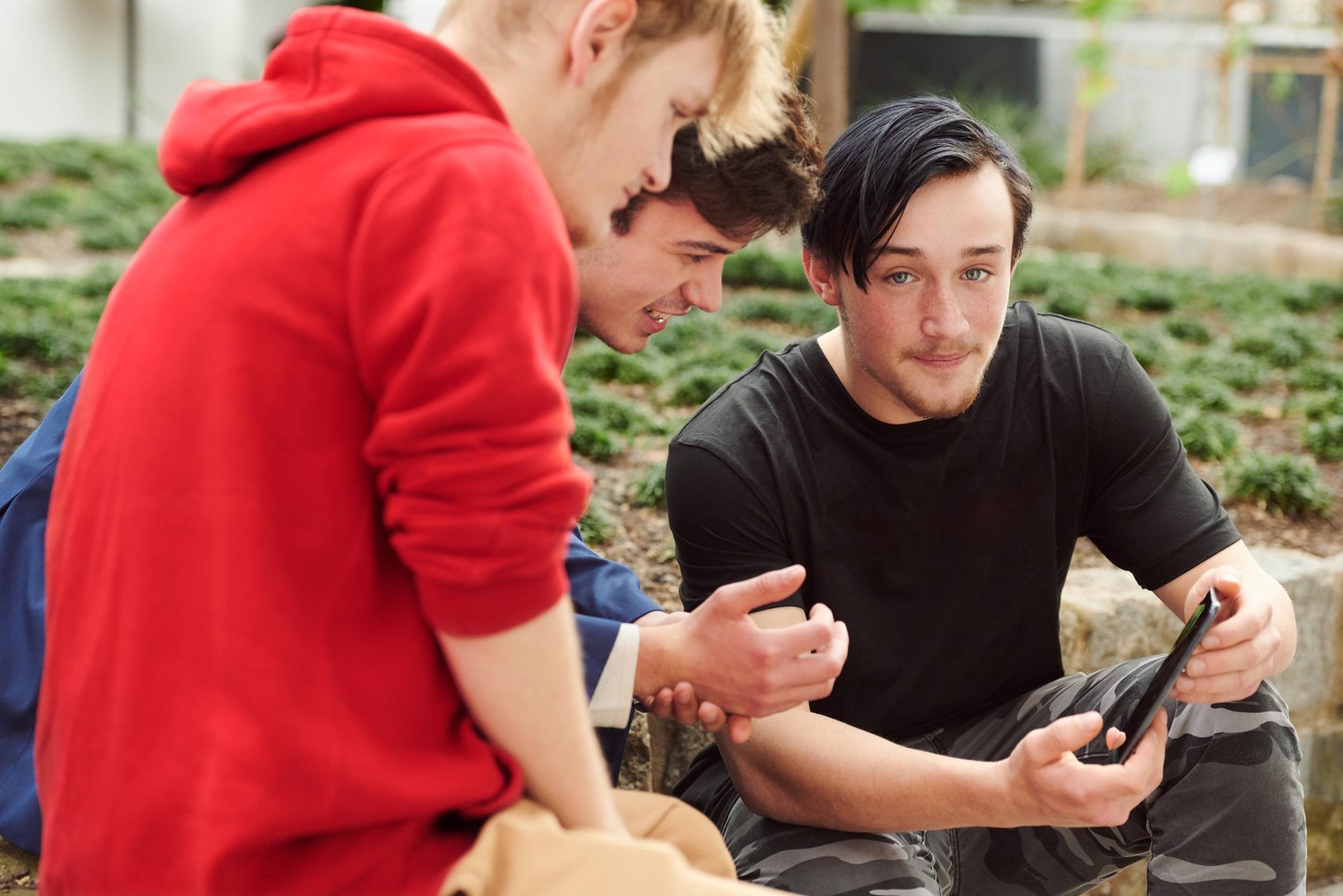 Drei junge Careleaver sitzen im Garten und schauen gemeinsam auf ein Smartphone