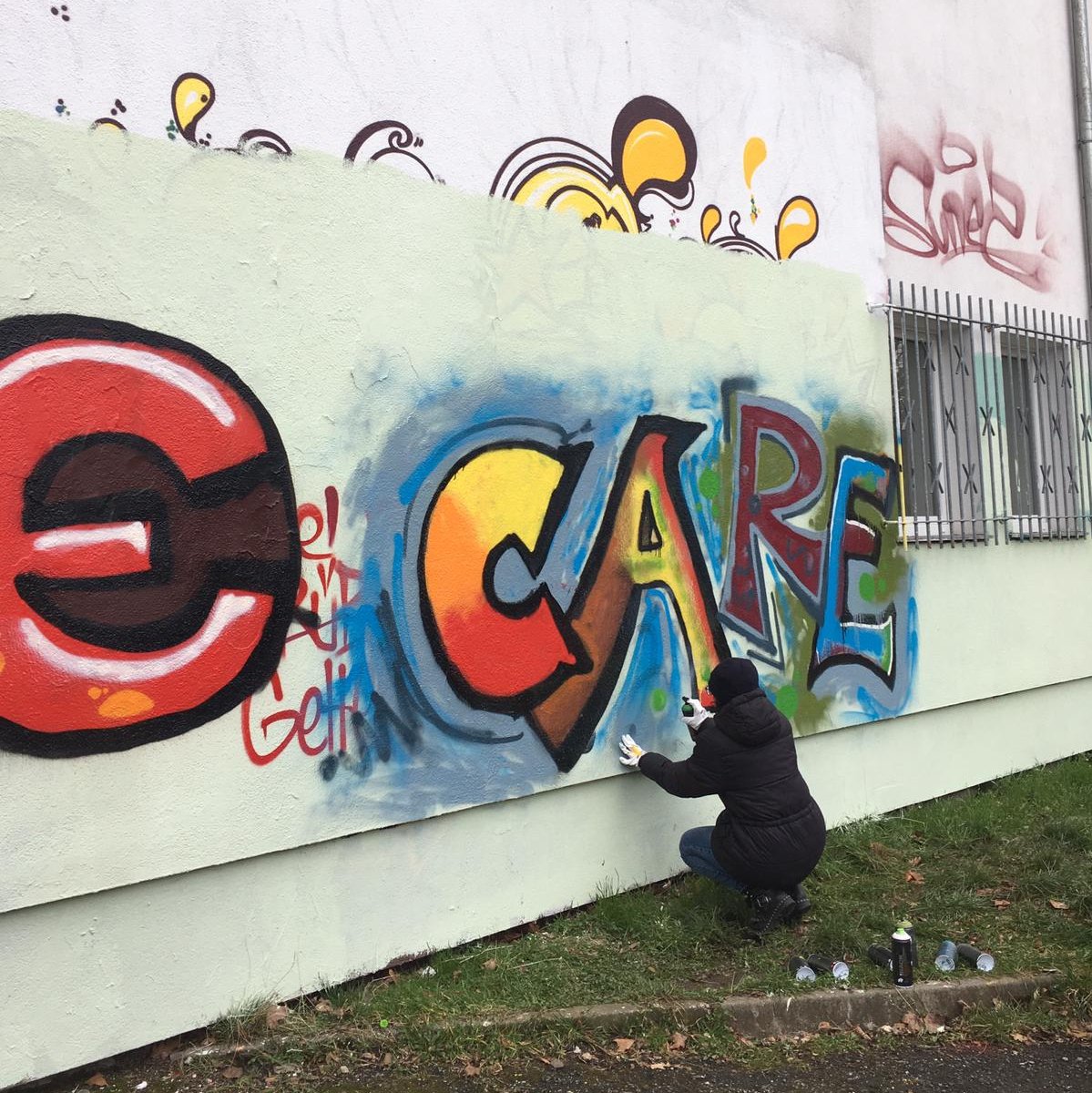 Eine Workshopteilnehmerin hockt vor einer Graffitiwand und sprüht das Wort CARE