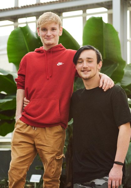 Zwei Kumpels blicken beim Fotoshooting im Botanischen Garten lachend in die Kamera
