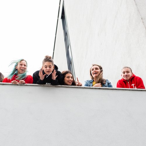 Sechs junge Careleaver blicken von einem Balkon hinunter Richtung Kamera